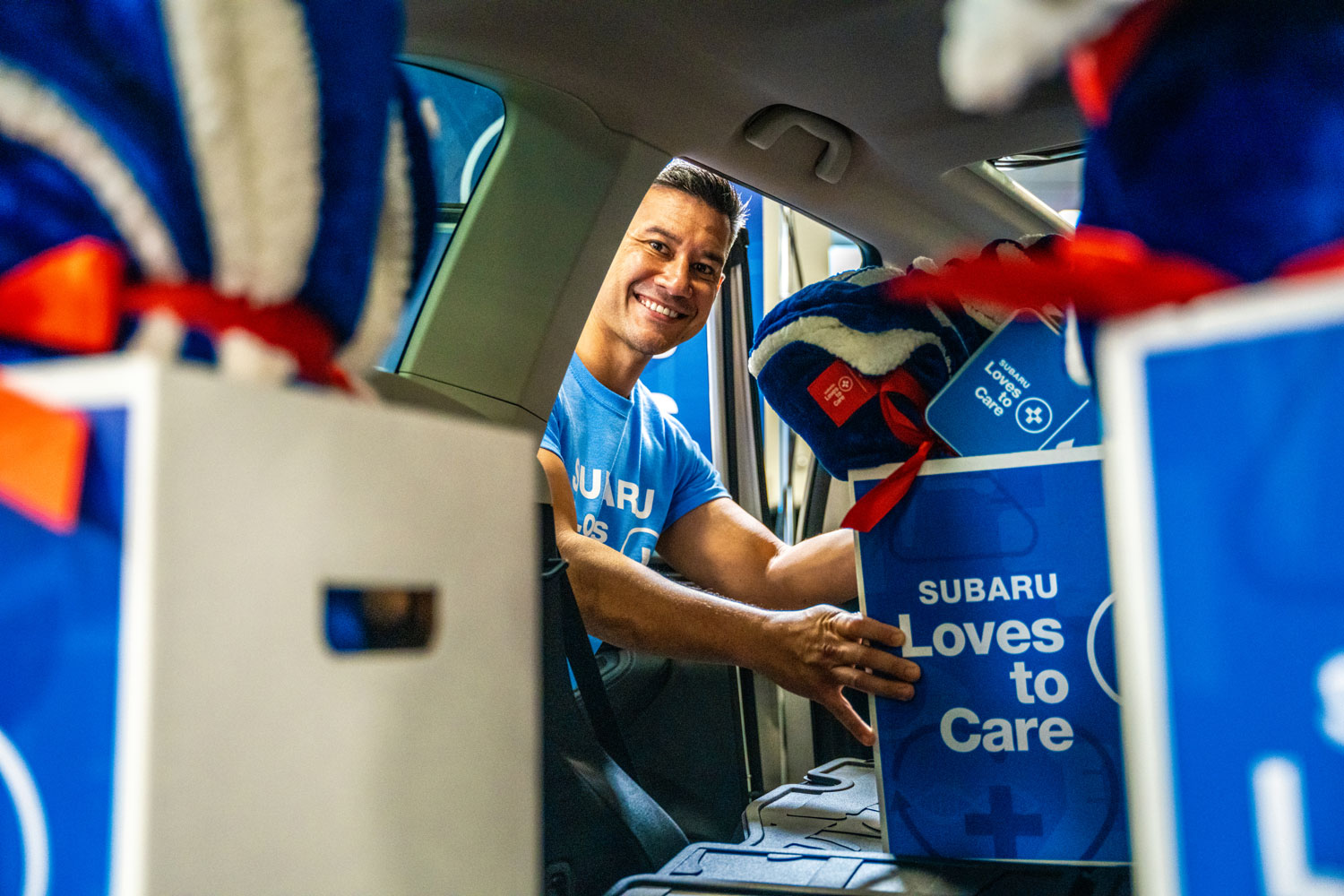 Smiling man in a blue Subaru shirt loads blue boxes labeled 
