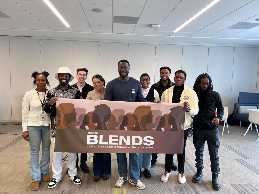 A diverse group of nine people smiling, holding a