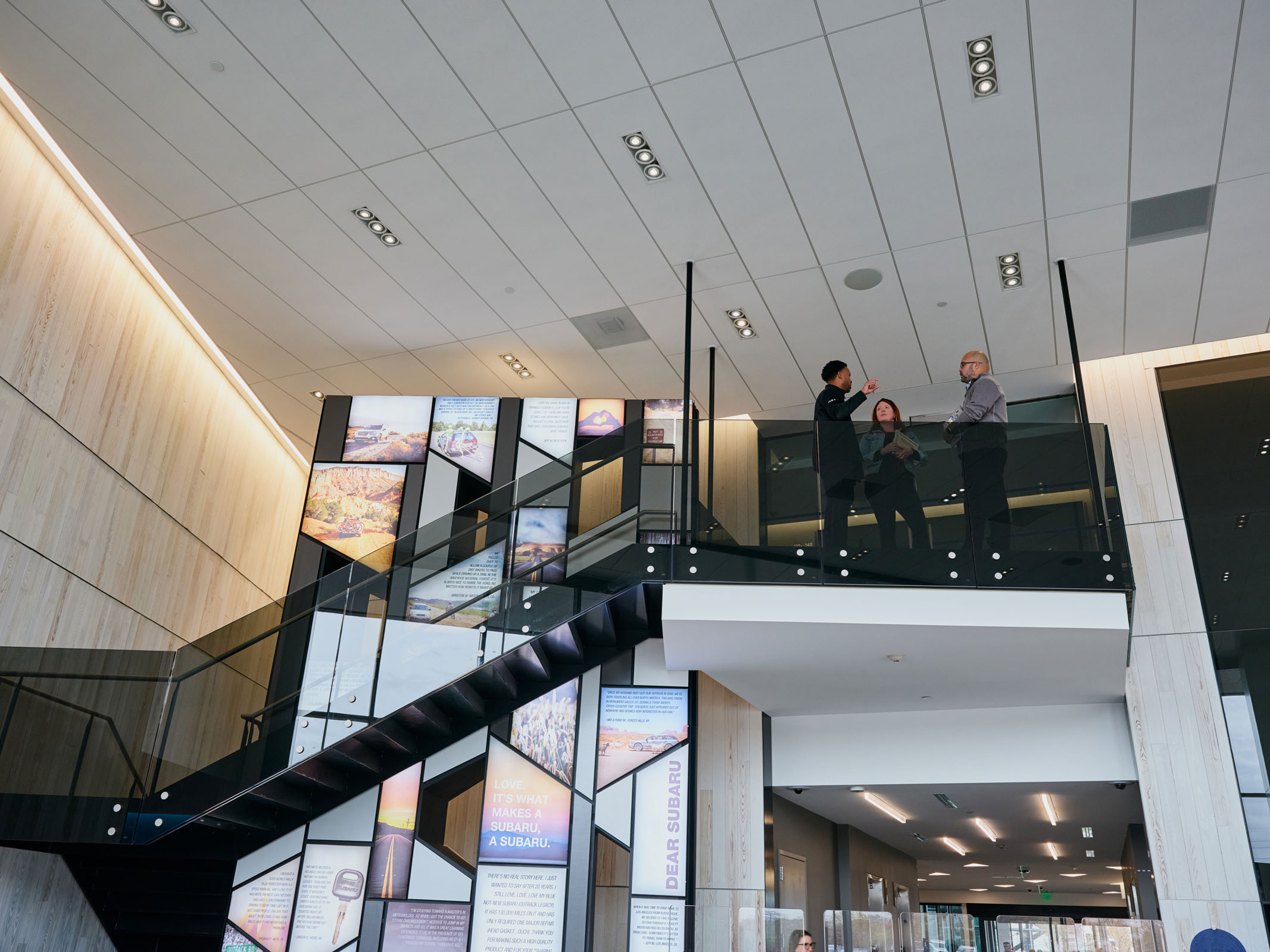 Three people engaged in conversation stand at the top of stairs on a modern glass balcony.