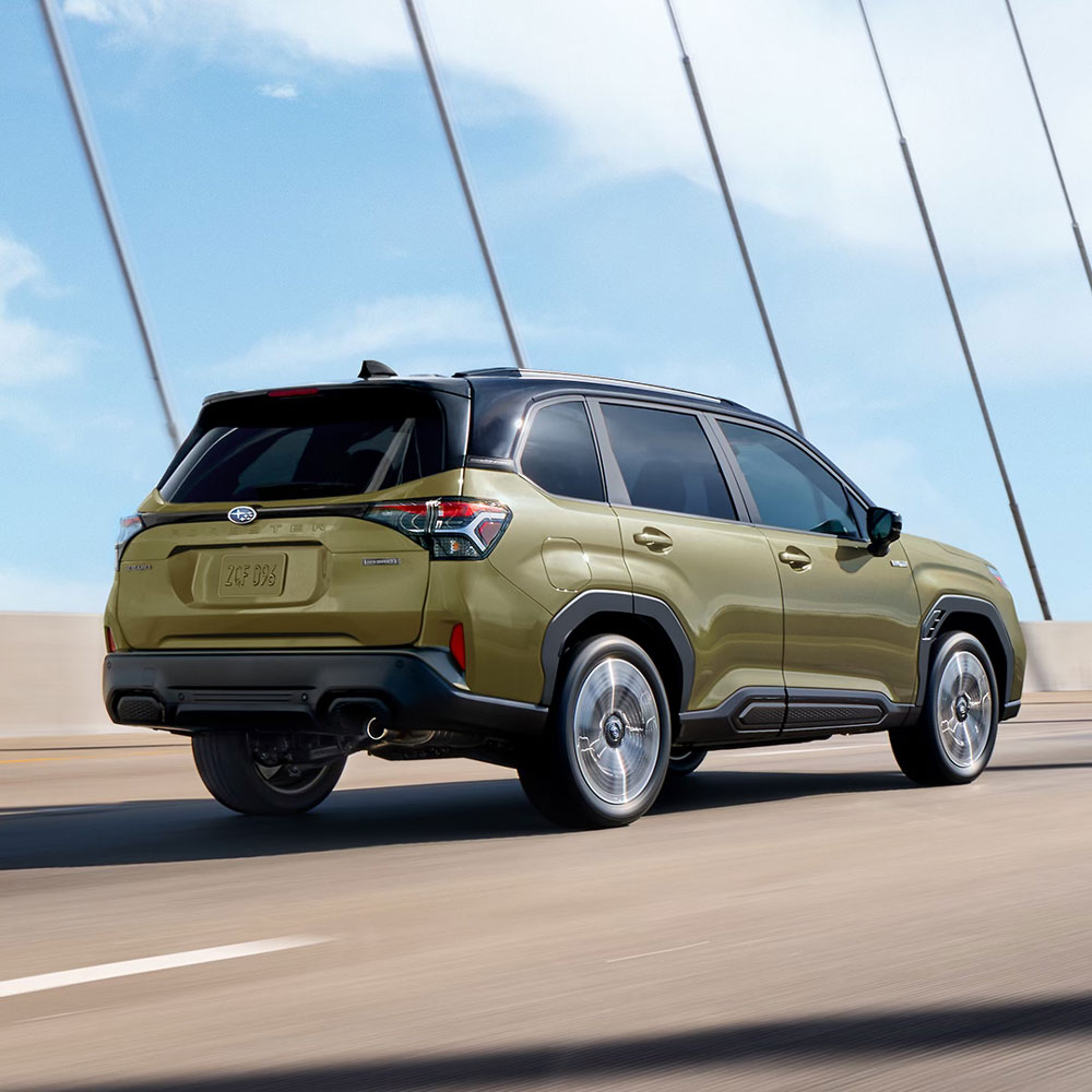 A green Subaru SUV drives on a sunny bridge, showcasing sleek design and modern features, with a vibrant blue sky in the background.