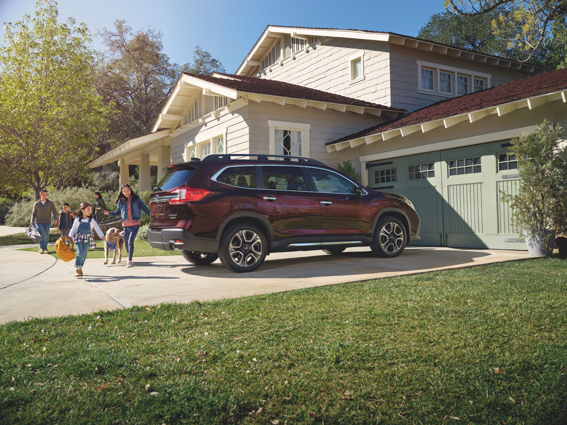 Family with a dog walks towards a burgundy SUV parked in a sunny driveway. A modern two-story house and green lawn set a cheerful, suburban scene.