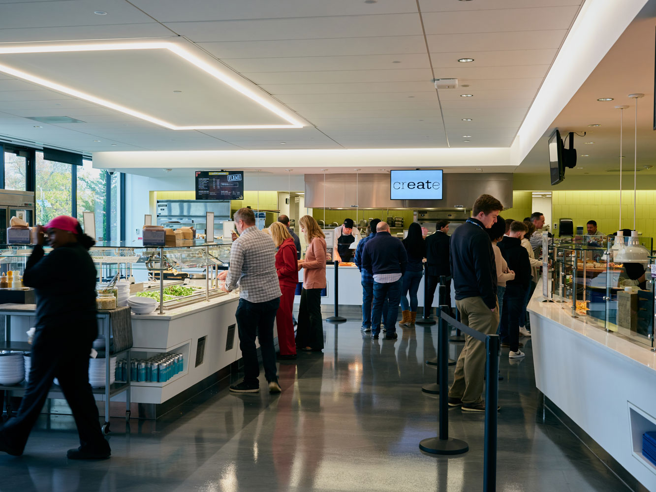 A busy cafeteria scene with people in line, selecting food from counters.