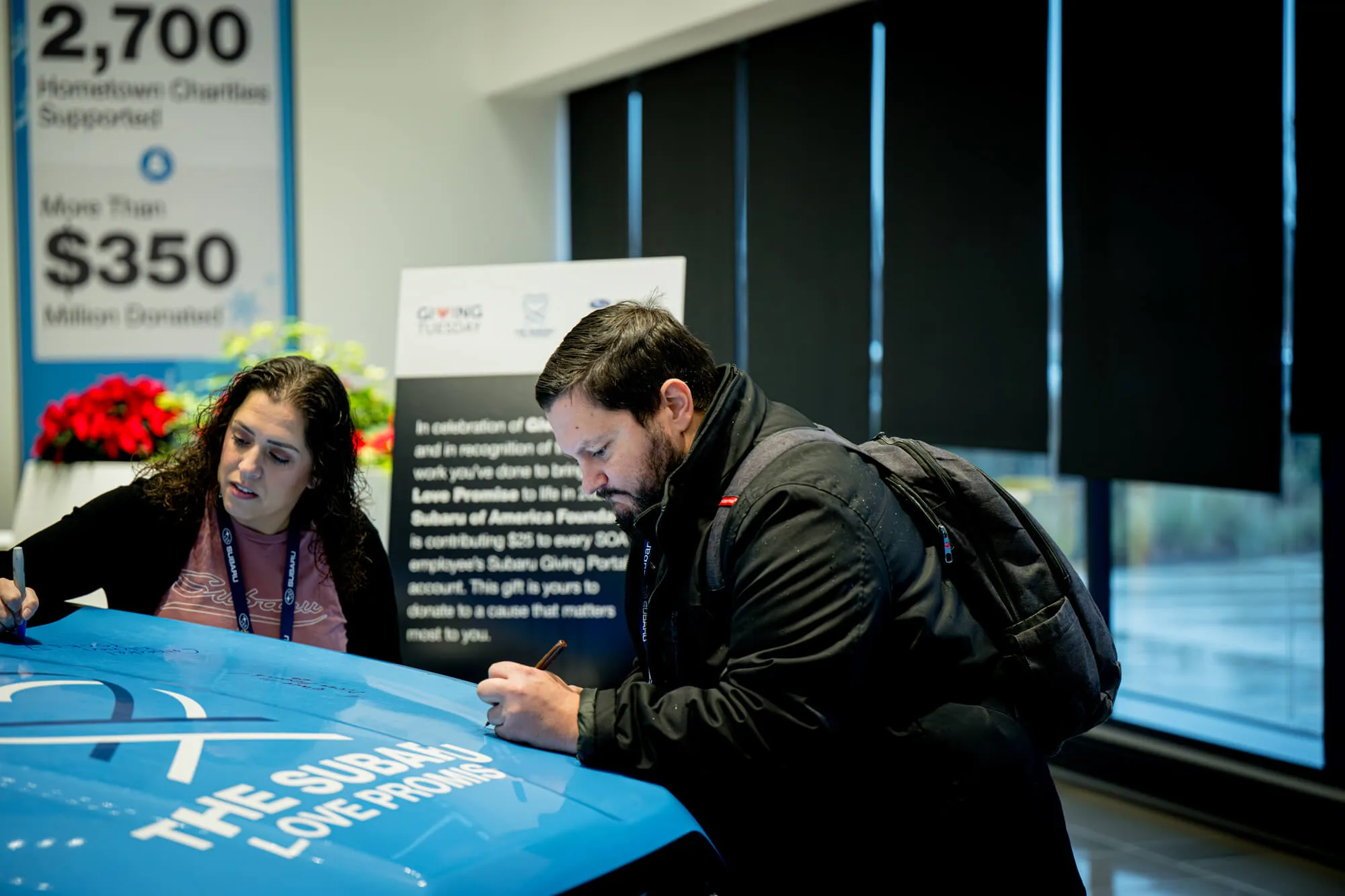 People signing a Subaru Love Promise vehicle during a community giving event.