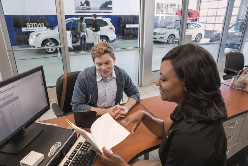 Subaru retailer employee reviewing paperwork with a customer in a dealership.