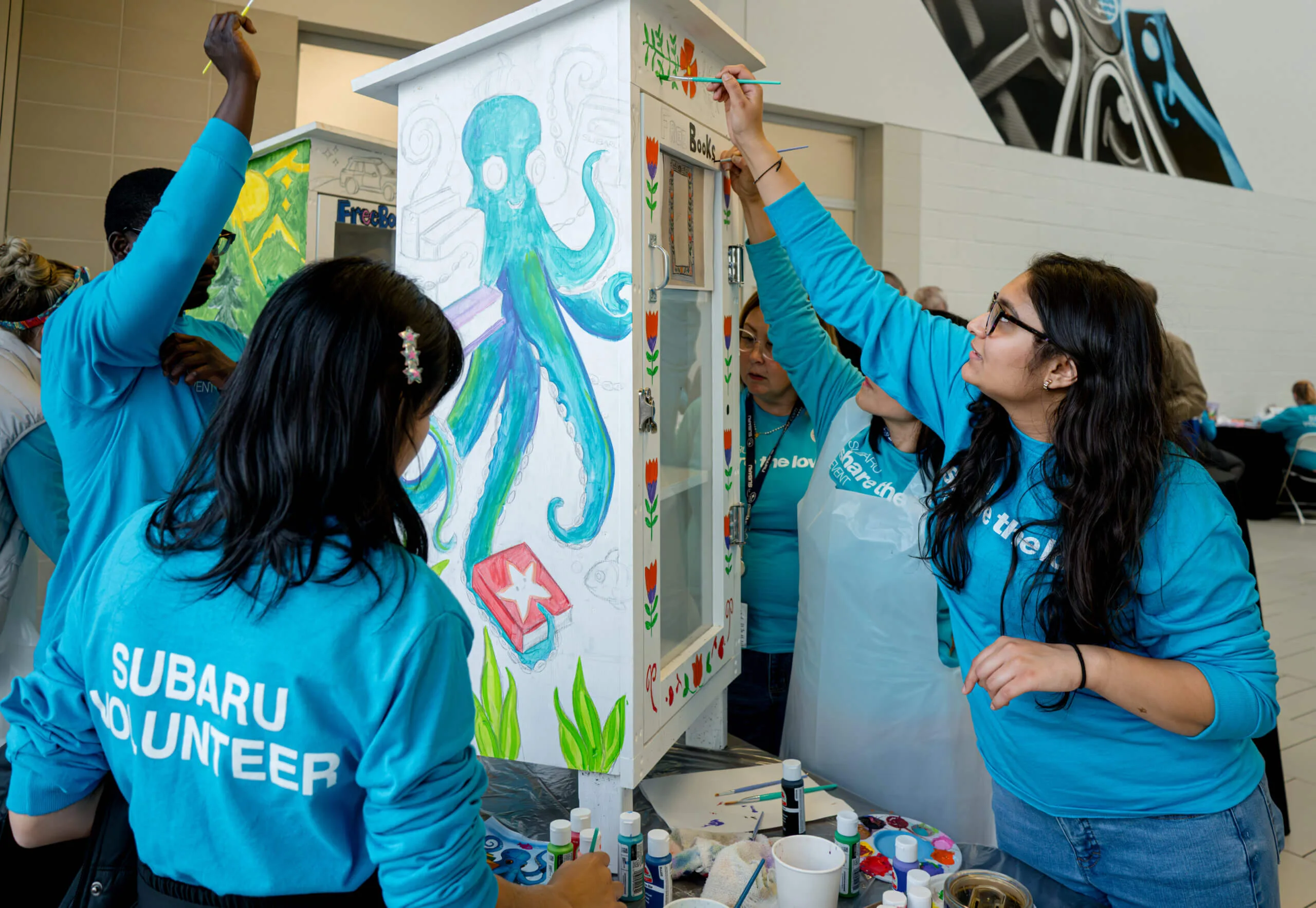 Subaru volunteers painting a community book exchange cabinet.
