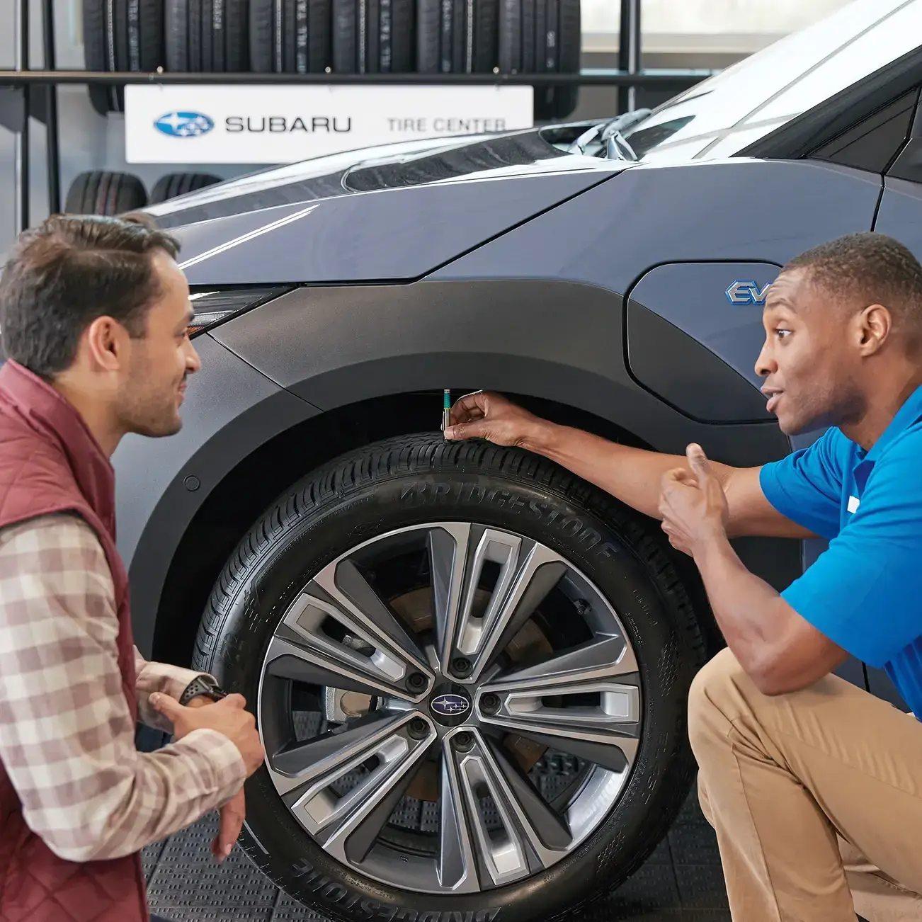A dealer and a customer inspecting a Subaru's tires.