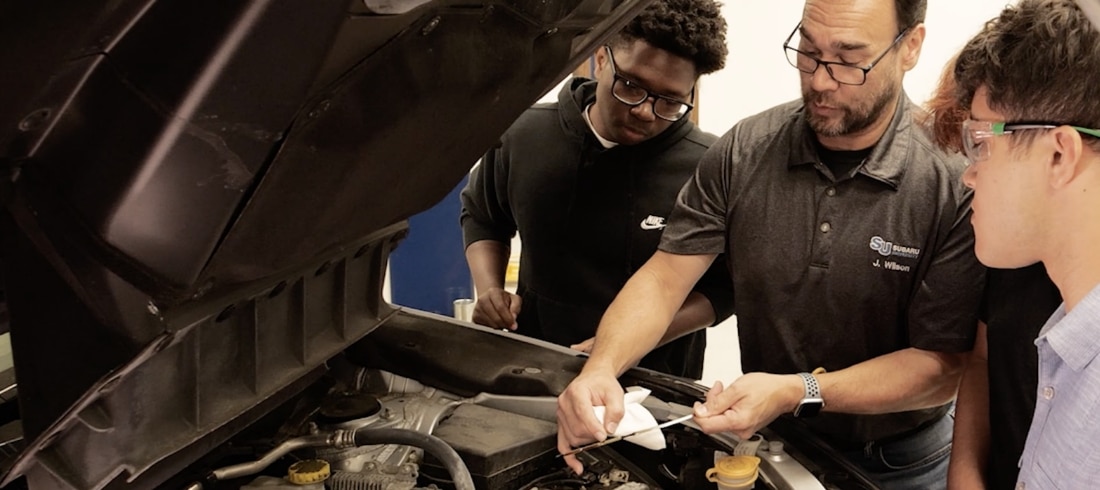 Mechanic and students looking in engine bay, teaching how to check fluids in a Subaru